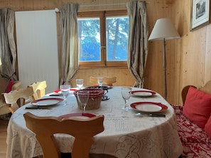 Comedor con una mesa dispuesta para cuatro, sillas de madera, una ventana con cortinas y una lámpara.