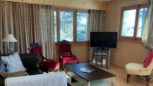 A living room with a sofa, armchairs, a coffee table, a TV on a stand, and a window with curtains. - chalet with breathtaking views of the alps (Crans-Montana)