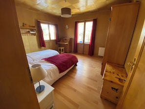 A bedroom with a bed, a desk, a wardrobe, and a window.