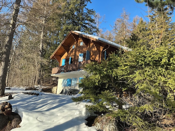 A wooden cabin with a balcony, surrounded by trees and snow.