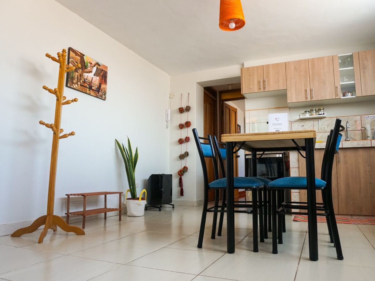 A dining area with a wooden table and chairs, a coat rack, a potted plant, and a small bench.