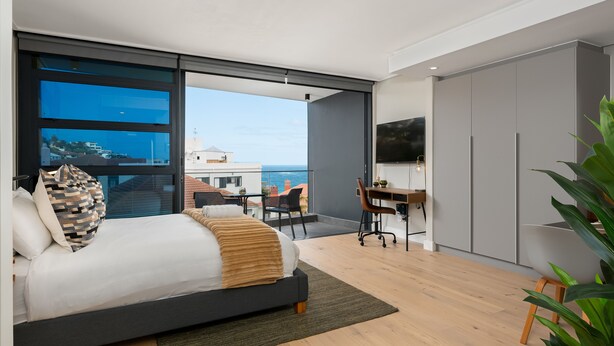 A modern bedroom with a large bed, a desk, and a TV. It has a balcony with a view of the sea. - 7 on Bantry 403 (Cape Town)