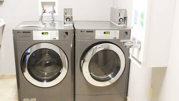 Two stacked front-loading washing machines in a laundry room with a white tiled floor and a door on the right.