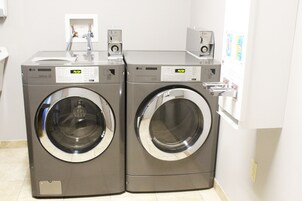 Two stacked front-loading washing machines in a laundry room with a white tiled floor and a door on the right.