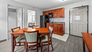 A compact kitchen with wooden cabinets, a refrigerator, and a microwave. There is a dining table with chairs and a rug on the floor. - Independence Stay Hotel & Suites (Marinette)