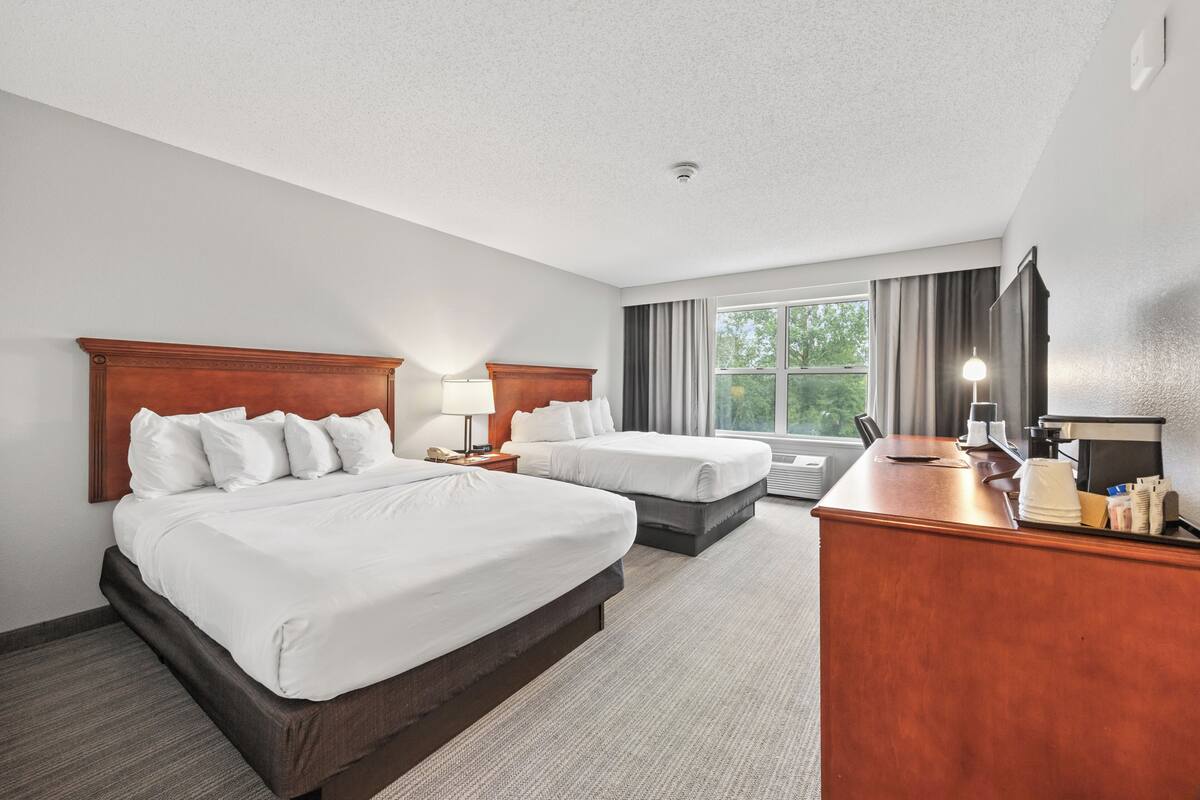 A hotel room with two beds, a desk, a lamp, and a window with curtains.