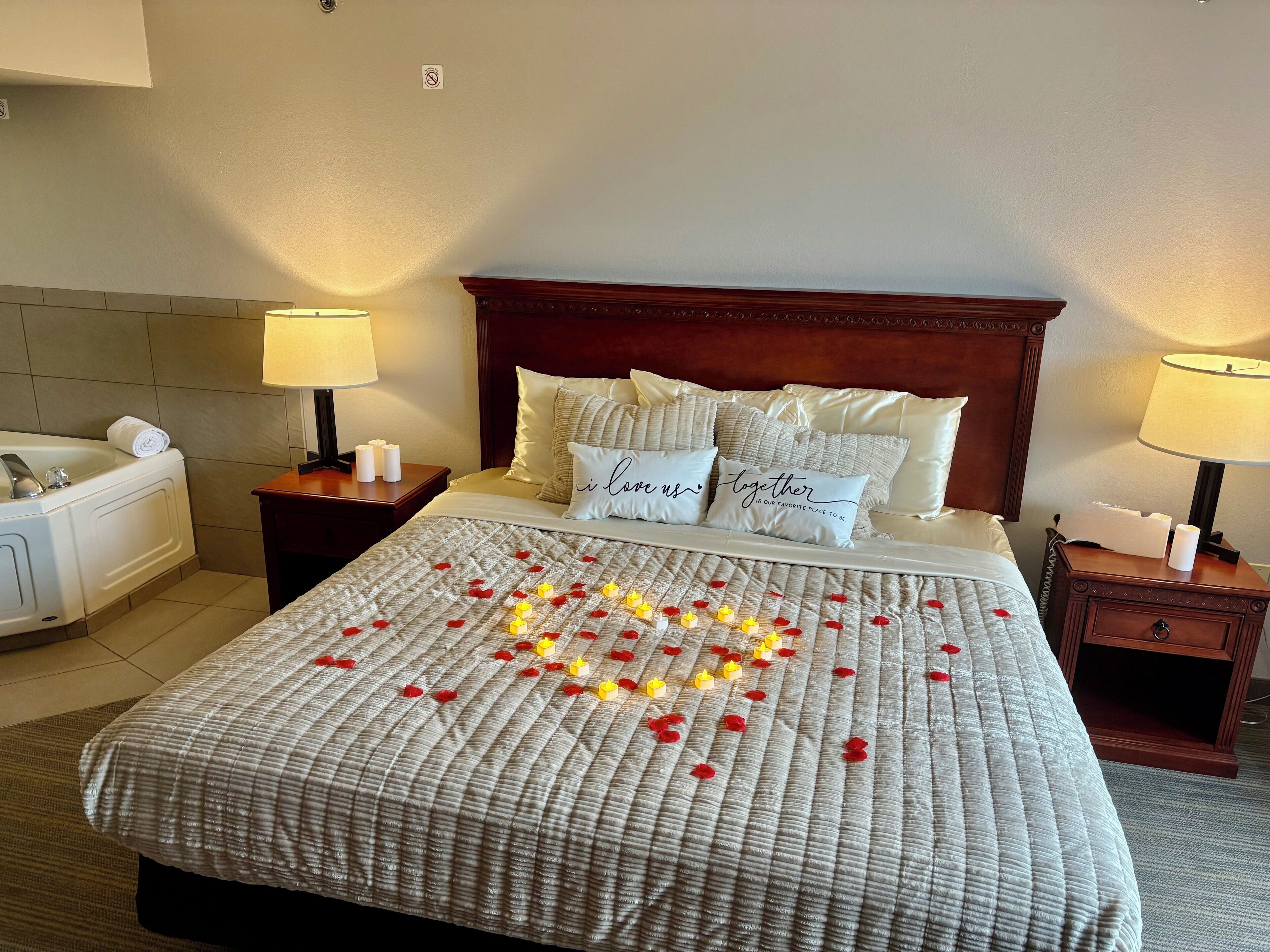 A hotel room with a bed, two bedside tables, a nightstand, a lamp, a towel, and a bath tub.
