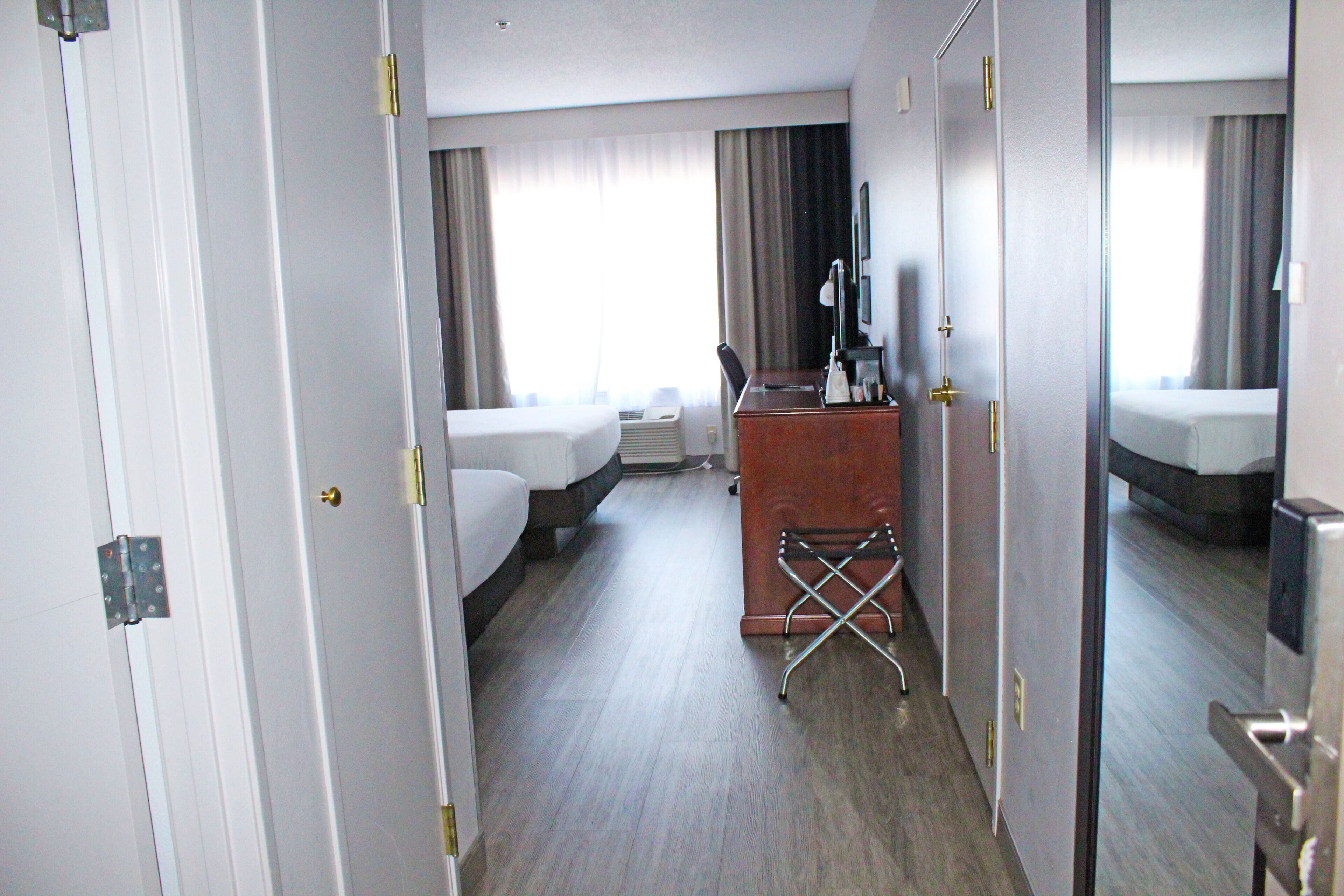 A hotel room with a bed, a desk, a chair, and a mirror.