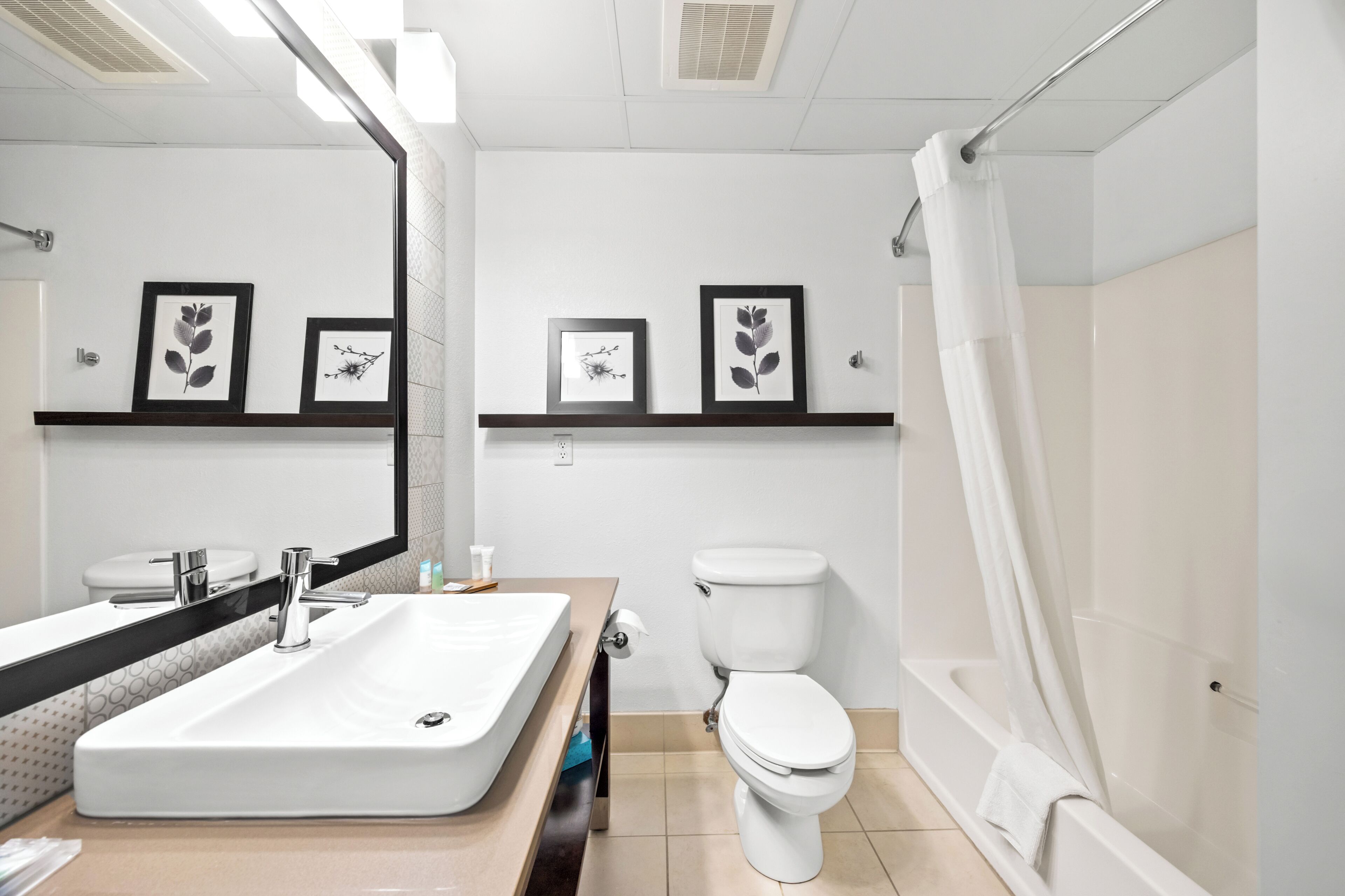 Un baño moderno con un lavamanos grande, inodoro y bañera. Hay cuadros enmarcados en la pared y una toalla colgando de la bañera.