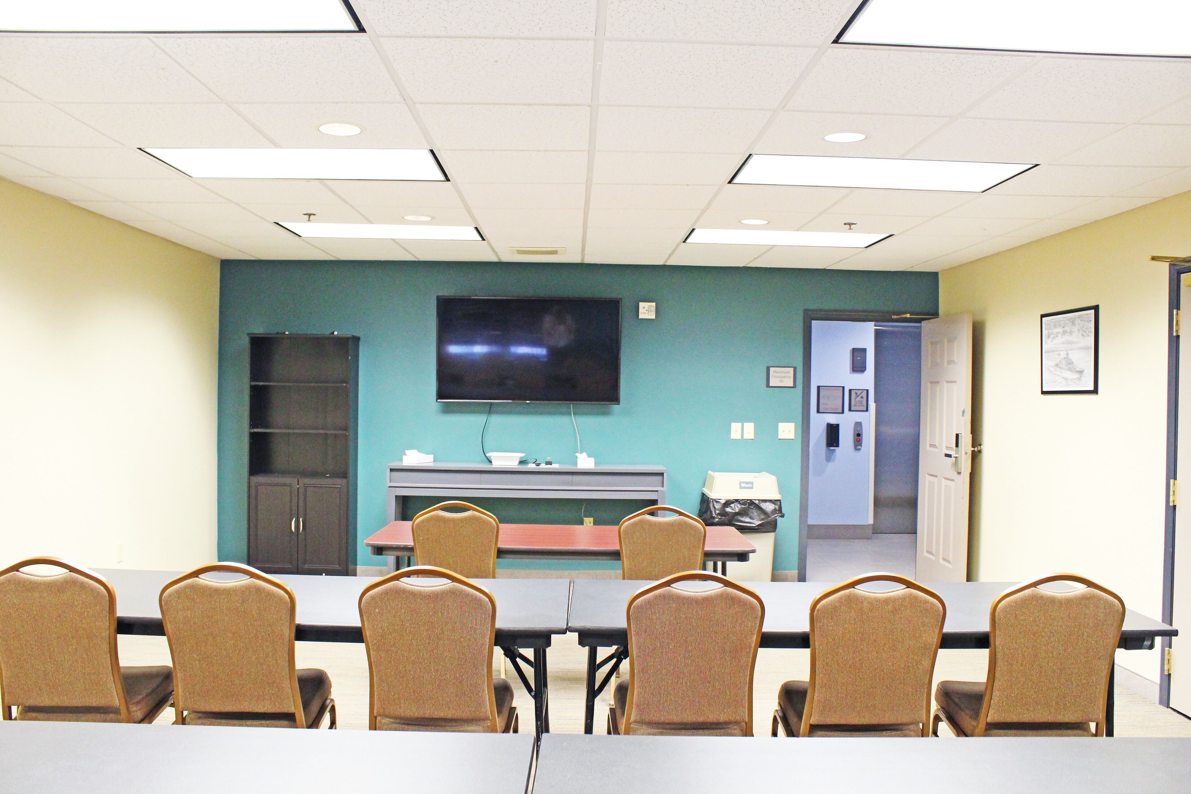 A conference room with a long table, six chairs, a TV screen, a whiteboard, and a door leading to another room.