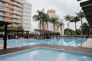 A swimming pool with a wooden deck, surrounded by palm trees and a multi-story building with balconies. - La Bete Nautilus Ap Beto Carrero (Penha)