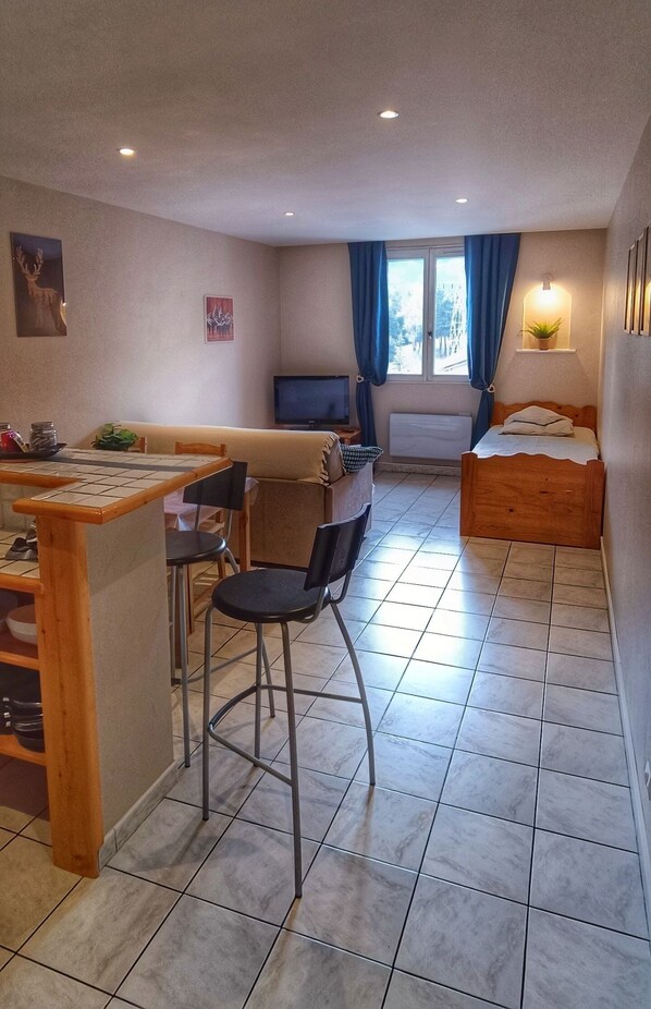 A compact room with a kitchenette, a bed, a TV, and a window with curtains.