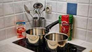A kitchen with two stainless steel pots on an induction cooktop, a box of tomato soup, and a package of Fiorini pasta. - Grand Studio 3 Personnes Idéalement Placé (Barcelonnette)