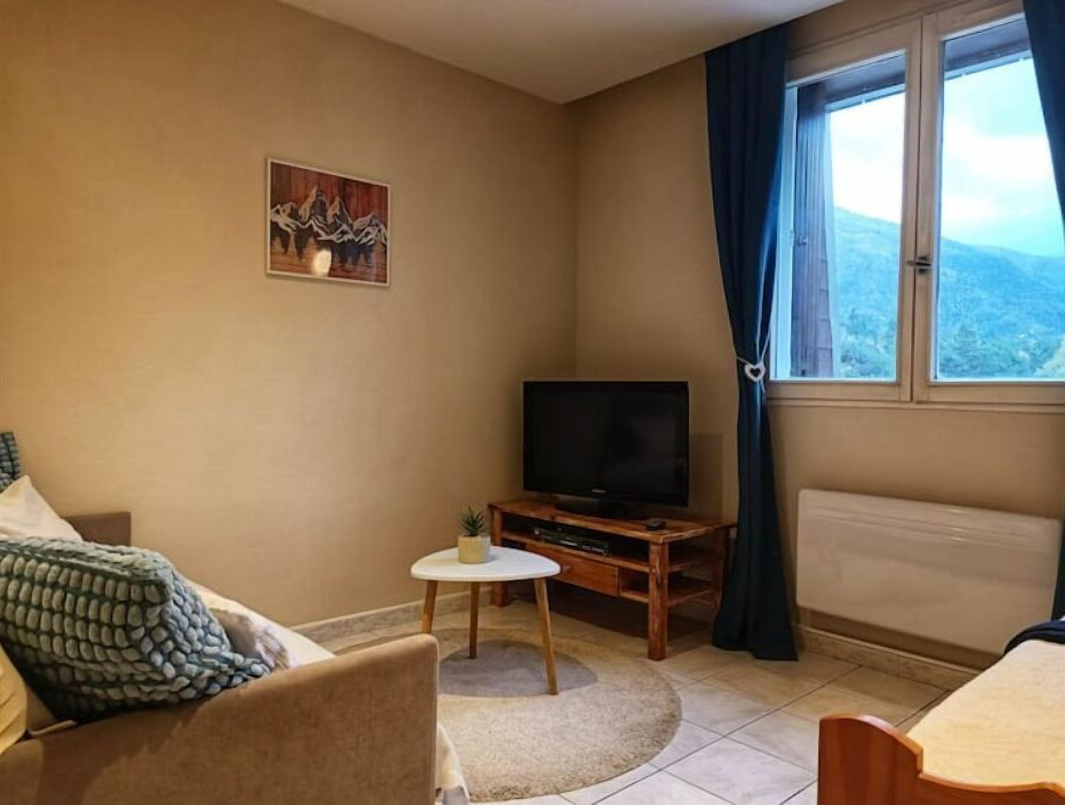 Una sala de estar con televisor, una mesita, sofá y una ventana con cortinas.