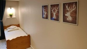 A bedroom with a wooden bed, a wall-mounted shelf with a plant, and three framed deer head pictures. - Grand Studio 3 Personnes Idéalement Placé (Barcelonnette)