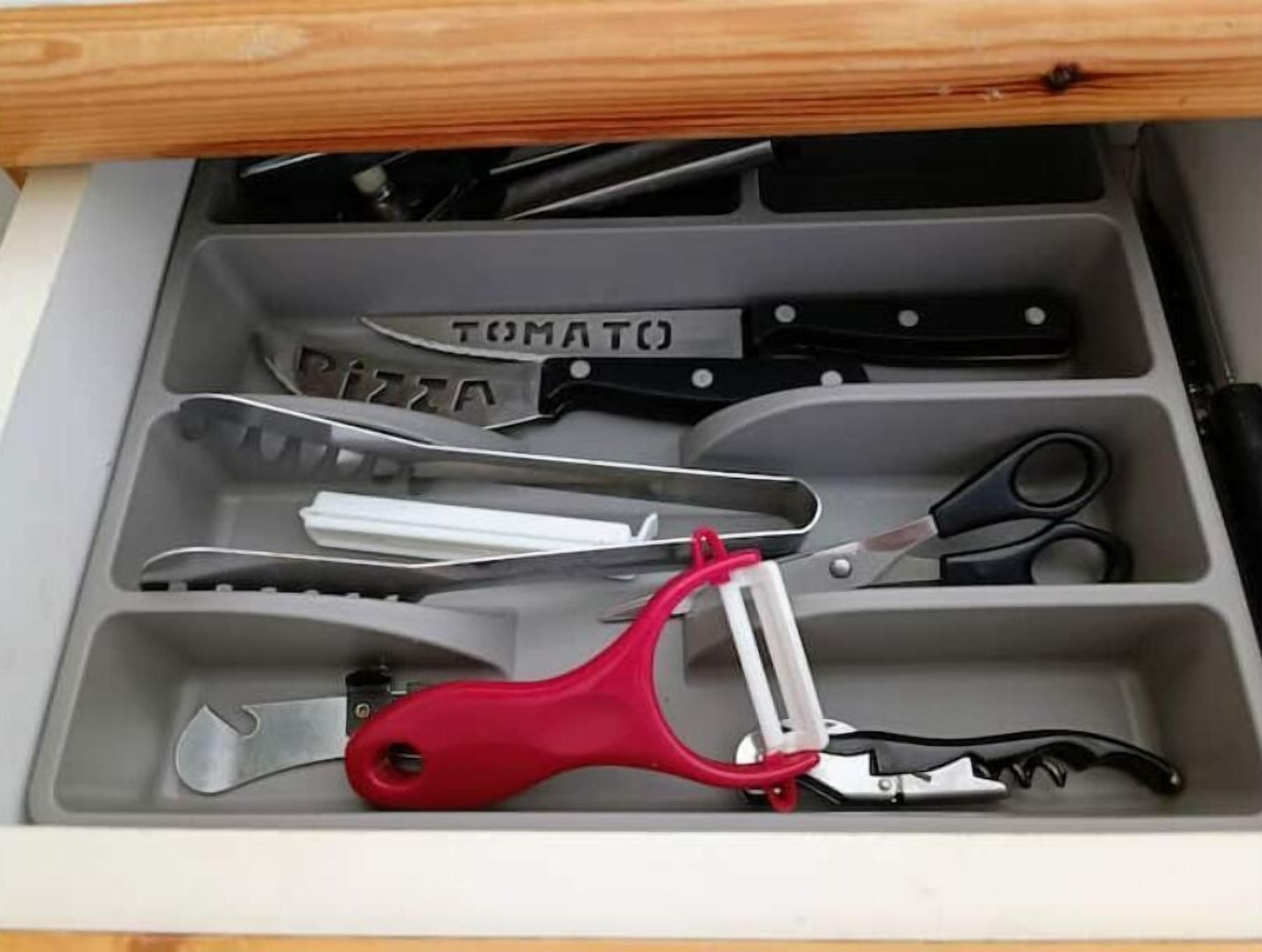 A drawer with compartments containing various kitchen utensils, including a pizza cutter and a tomato knife.