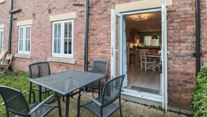 A brick building with a patio area featuring a table and chairs, a sliding glass door leading to a kitchen, and a small outdoor seating area.