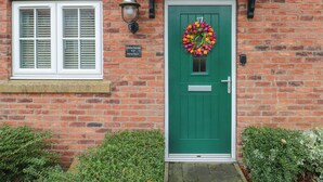 A green door with a wreath, a window with shutters, and a brick wall.