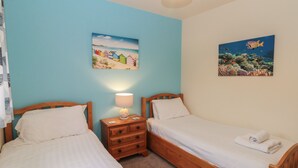 A bedroom with two single beds, a nightstand with a lamp, and two wall art pieces depicting beach and underwater scenes.