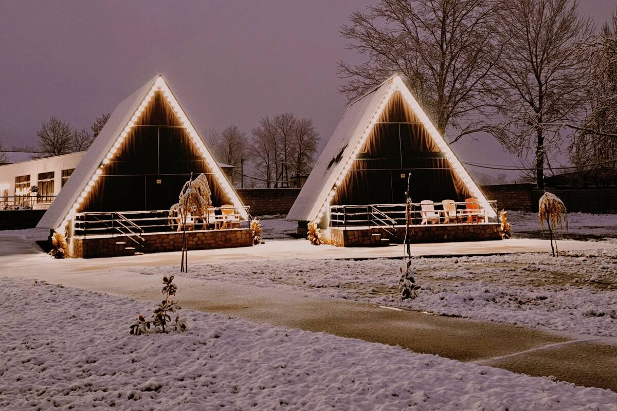 Two triangular-roofed buildings with a snow-covered ground, a clear sky, and leafless trees in the background.