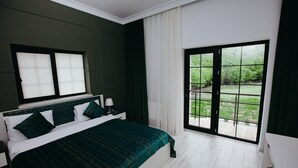 Un dormitorio con una cama grande, una mesita de noche, una ventana con persianas, un cerramiento de vidrio corredero a un balcón y vistas a zonas verdes.