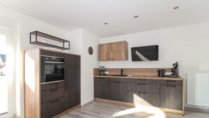 Una cocina moderna con armarios de madera oscura, horno empotrado y cafetera sobre la encimera.