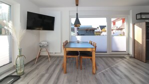 Una cocina moderna con una mesa de comedor, sillas, un televisor montado en la pared y vistas al exterior.