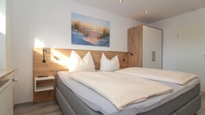Un dormitorio moderno con una cama grande, cabecera de madera y un cuadro de una puesta de sol sobre el agua.