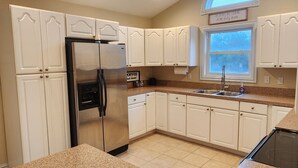 A kitchen with white cabinets, a stainless steel refrigerator, granite countertops, and a window with a view. - Goldie St Retreat - Heart of KDH, hot tub, pet friendly, centrally located  (Kill Devil Hills)