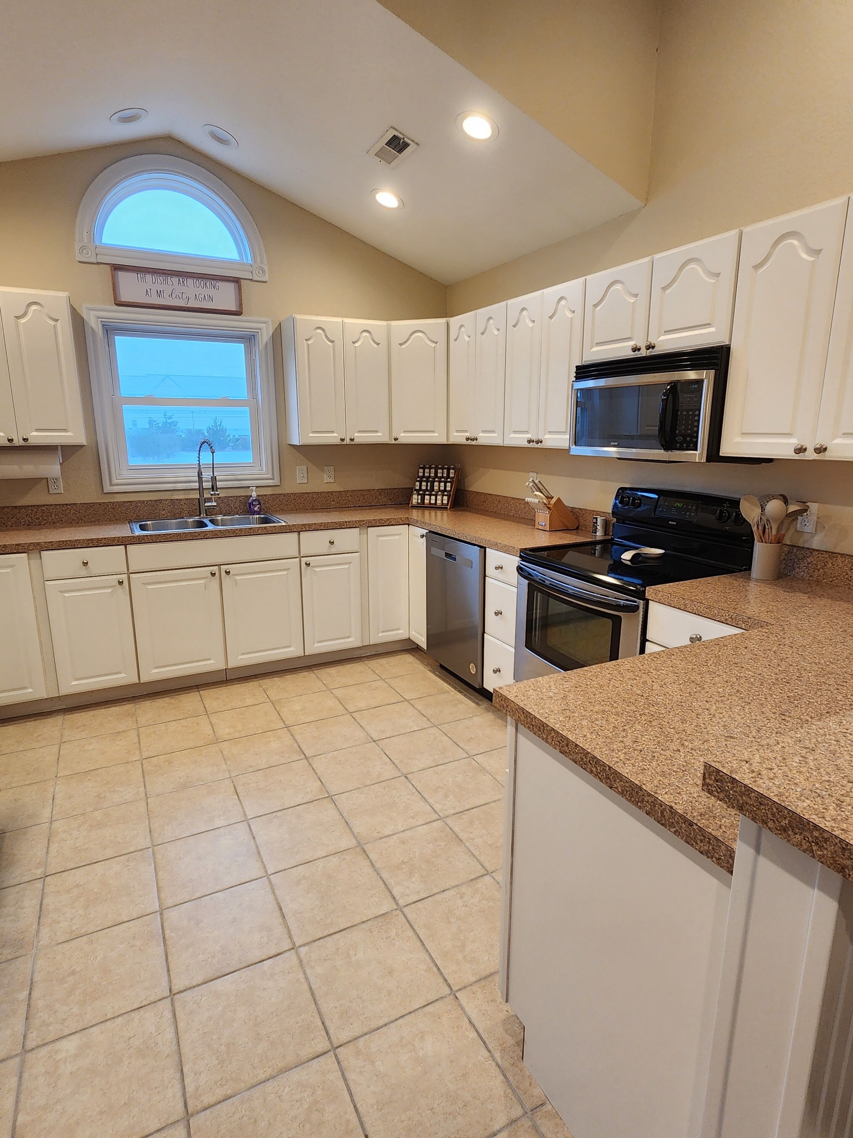 A kitchen with white cabinets, a stainless steel sink, a microwave, and a stove.