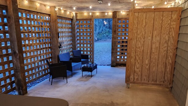 A cozy, enclosed patio area with a wooden ceiling, string lights, a table with chairs, and a wooden fence. - Goldie St Retreat - Heart of KDH, hot tub, pet friendly, centrally located  (Kill Devil Hills)