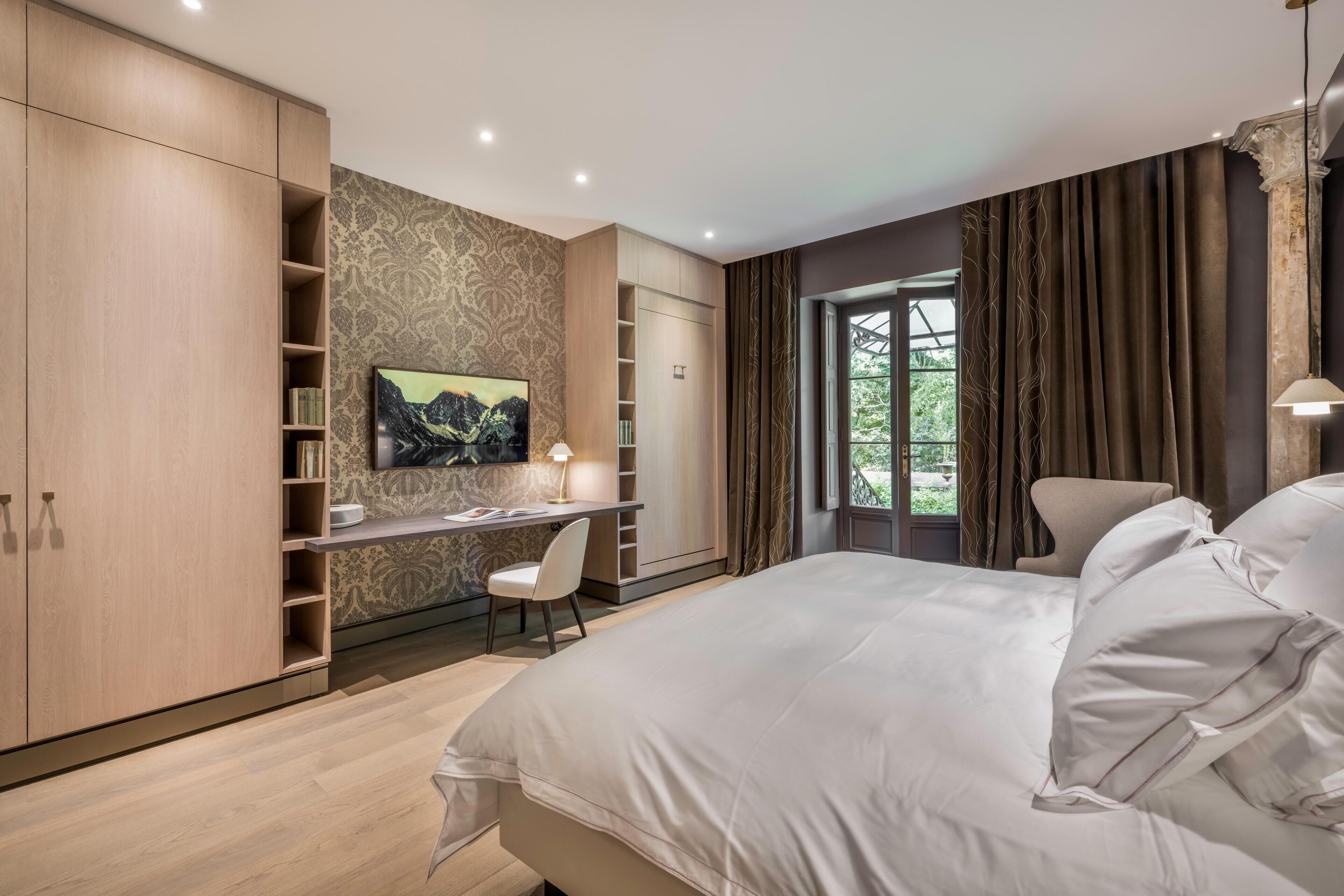 A modern bedroom with a large bed, a desk with a chair, and built-in wardrobes.
