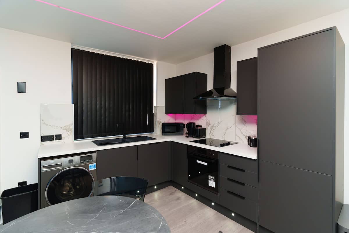 A modern kitchen with dark cabinetry, a built-in microwave, and a large window with blinds.