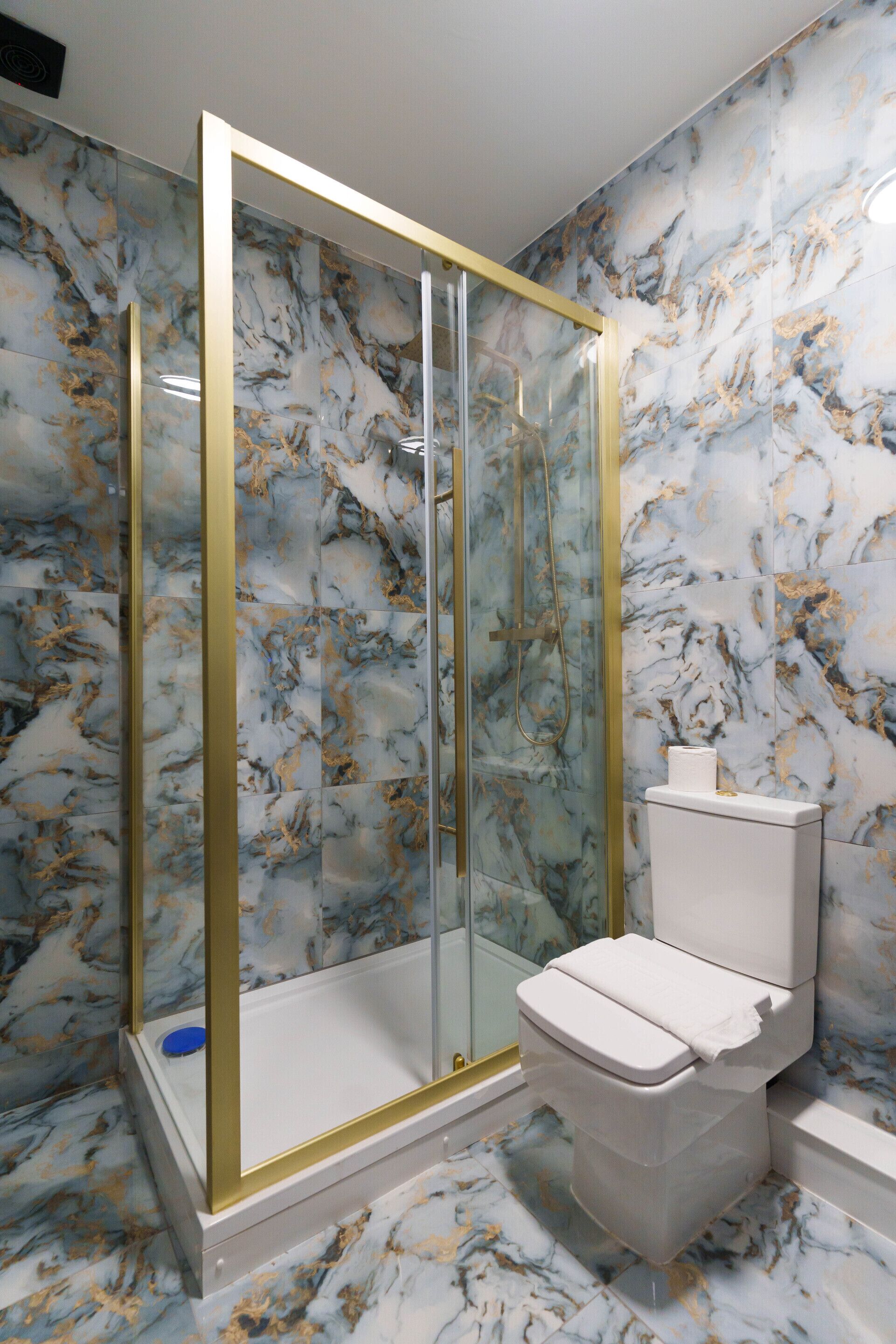 A bathroom with a marble floor, a glass-enclosed shower, and a toilet.