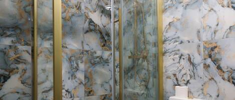 A bathroom with a marble floor, a glass-enclosed shower, and a toilet.