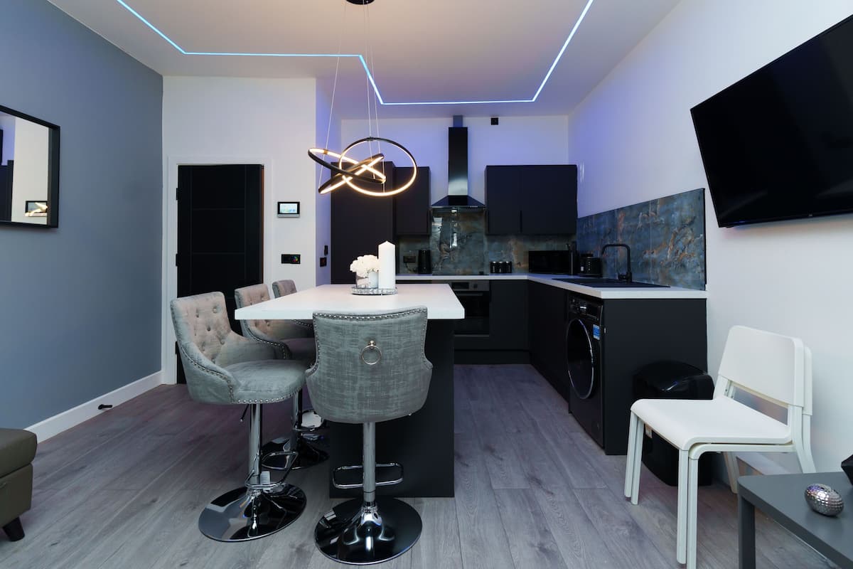A modern kitchen with a central island, bar stools, a flat-screen TV, and a dining table.