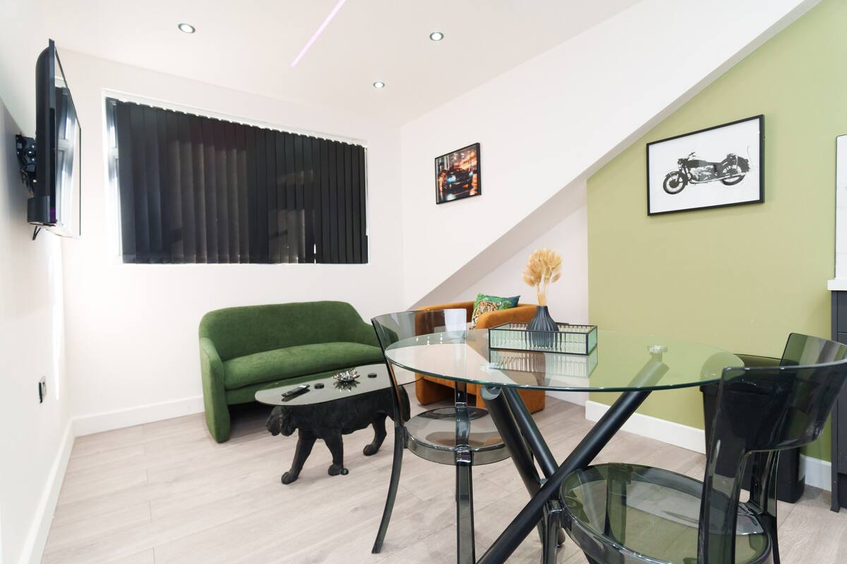 A modern living room with a green sofa, a glass coffee table, and a black cat statue.