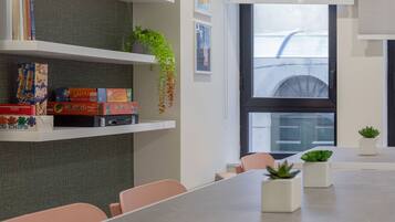 A modern conference room with a long table, several chairs, and shelves with books and board games.