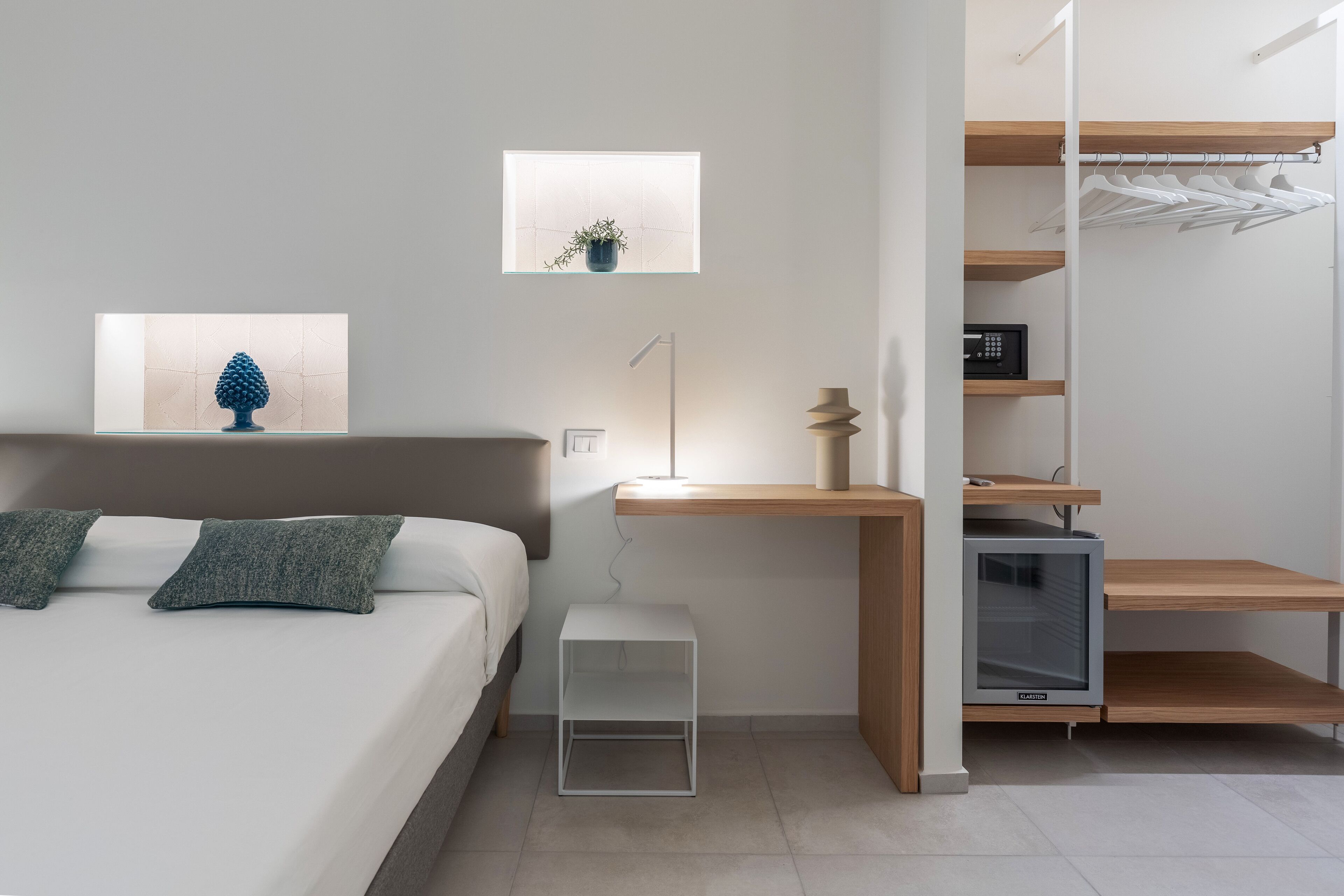 A modern bedroom with a bed, bedside table, lamp, and a built-in TV.