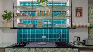 Eine Küche mit schwarzer Arbeitsplatte, einem Edelstahlspülbecken und einem eingebauten Backofen. Über der Arbeitsplatte befinden sich Regale mit Gläsern und Geschirr.