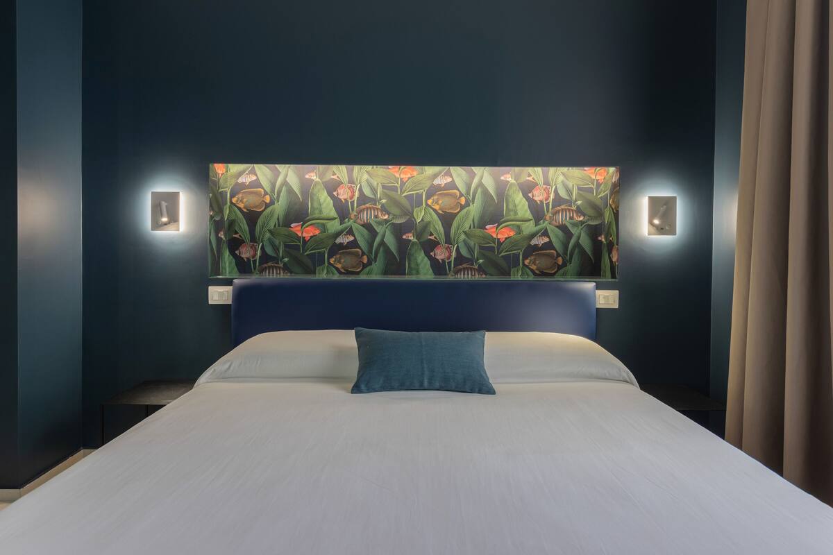 A bed with a blue headboard, a teal pillow, and a wall with a fish-themed painting.