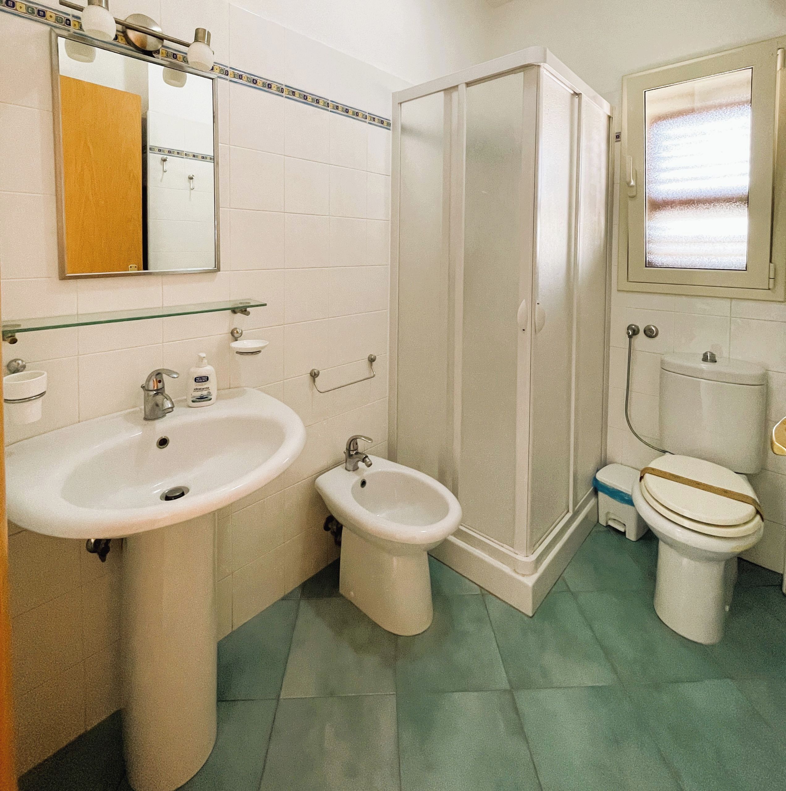 A bathroom with a sink, bidet, toilet, and a shower stall.