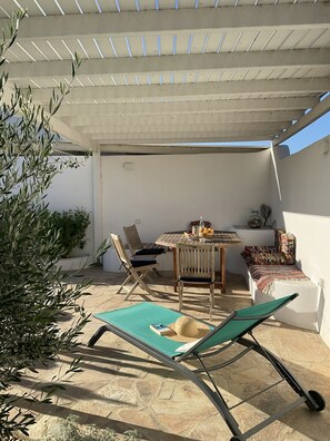 Eine überdachte Terrasse im Freien mit Tisch und Stühlen, einem Liegestuhl und einer kleinen Sitzecke mit Decke.