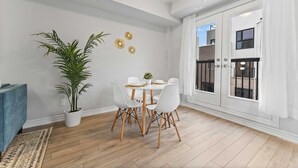 Et spiseområde med et rundt bord, hvide stole og en potteplante.