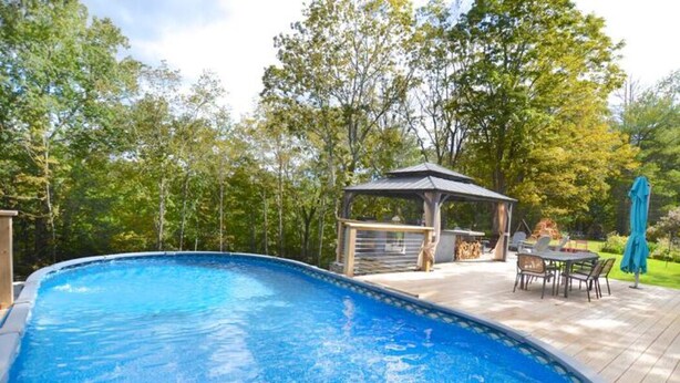 A swimming pool with a wooden deck, a gazebo, and outdoor furniture.