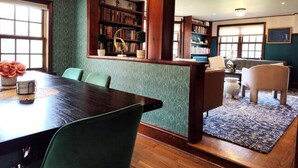 A dining area with a wooden table and chairs, a bookshelf, and a patterned rug.