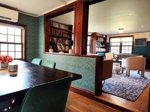 A dining area with a wooden table and chairs, a bookshelf, and a patterned rug.