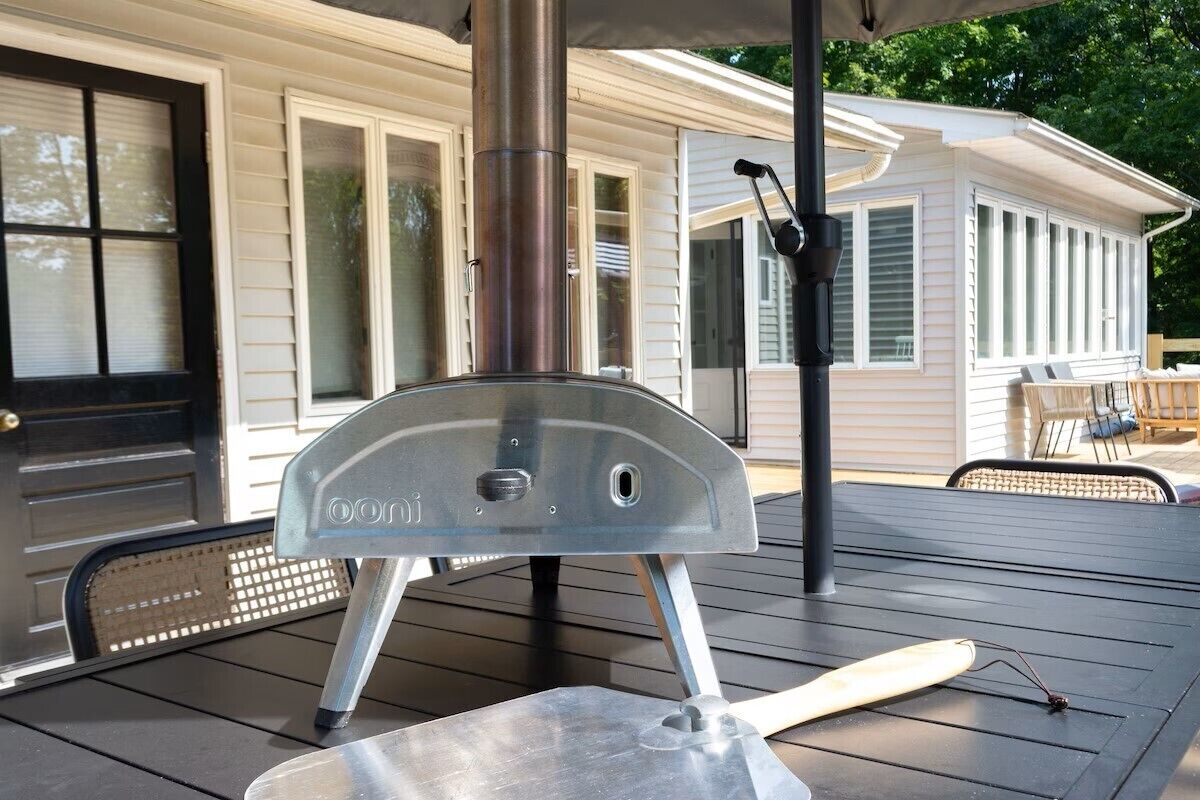 Ein tragbarer Grill auf einer Terrasse, im Hintergrund ein Haus.
