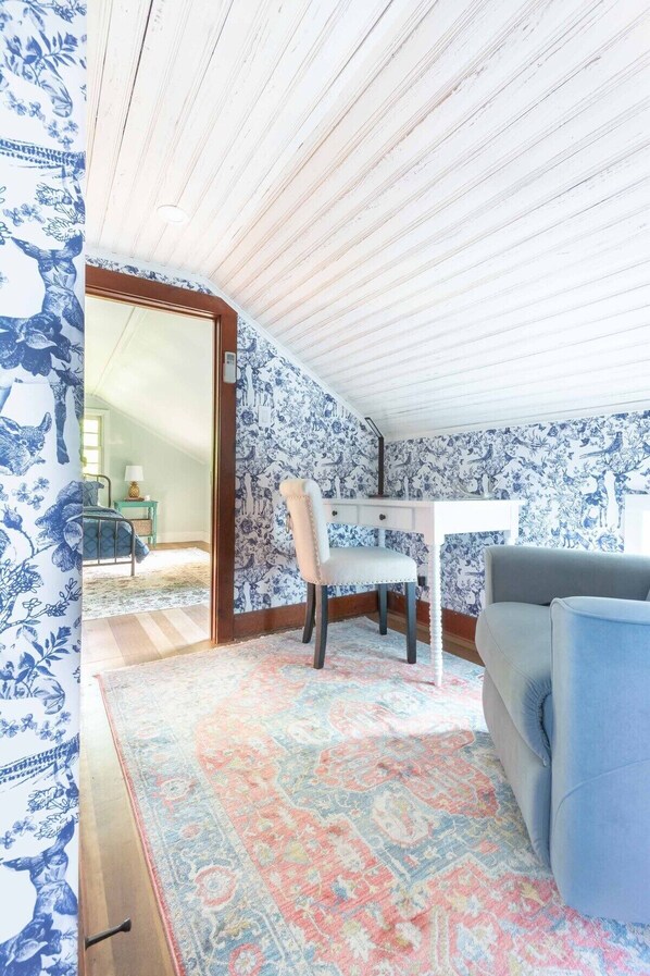 Une pièce avec un papier peint à motifs, un bureau blanc, une chaise bleue, un canapé bleu et un tapis à motifs.