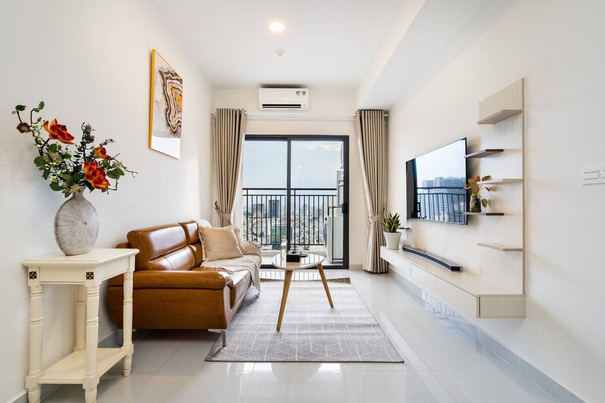 Una sala de estar moderna con un sofá, una mesa de centro, un televisor montado en la pared y un balcón con vista a la ciudad.